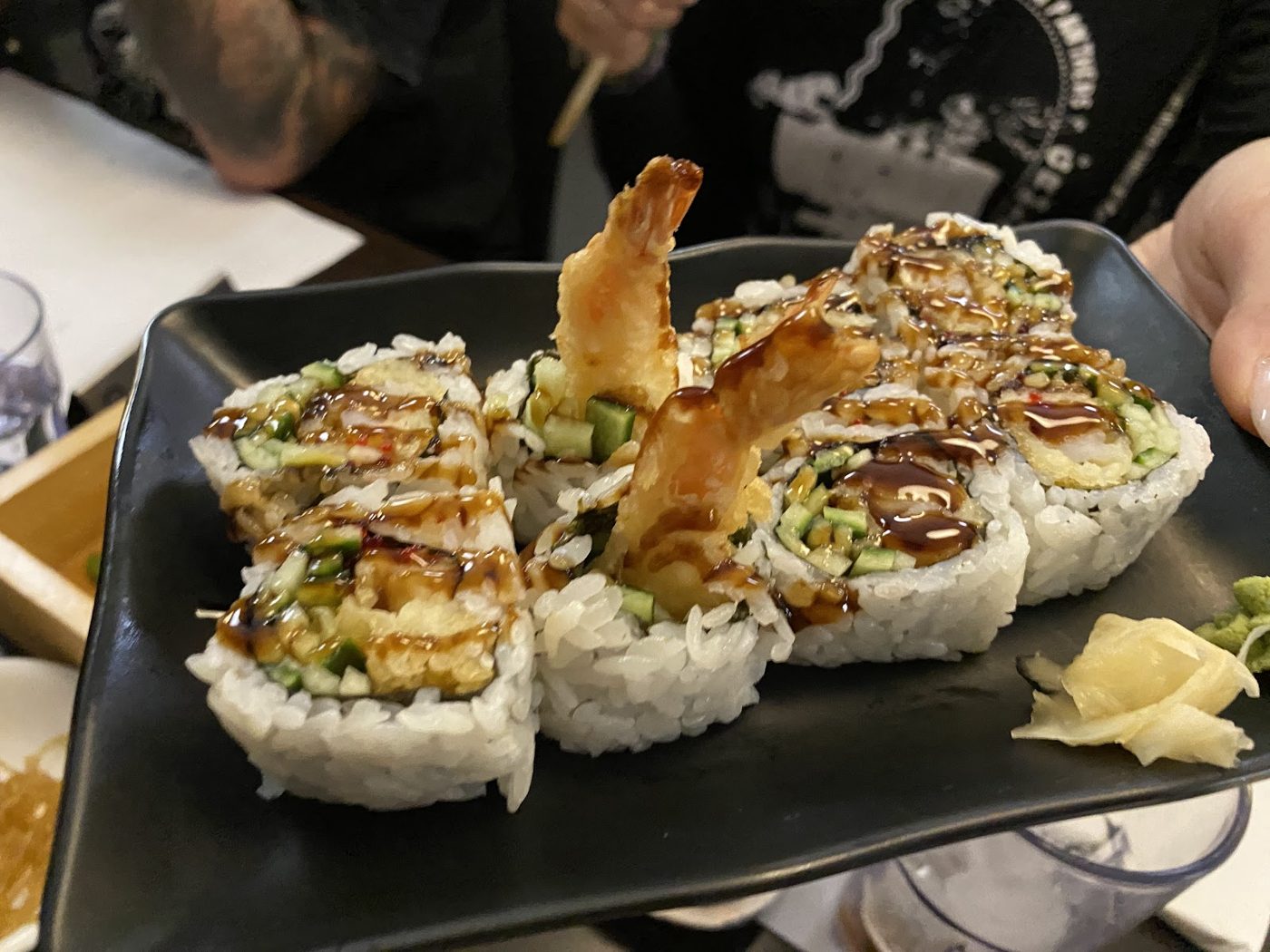 Rolls topped with shrimp tempura and sauce on a black plate